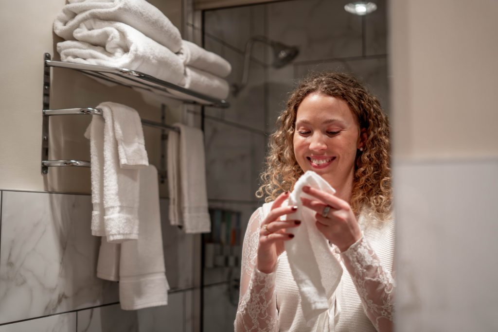 Woman cleaning her face in Steam Plant Hotel room bathroom amenities